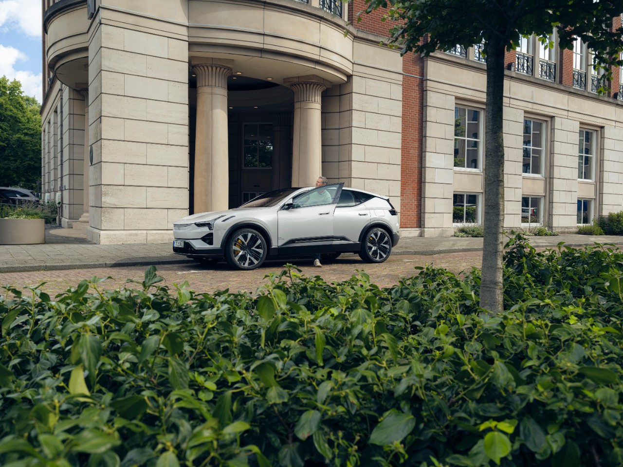Mann sitzt auf Fahrersitz eines stehendes Autos schaut auf sein Handy Fahrertuer steht offen.