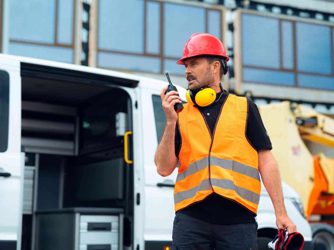 Person mit Funkgeraet und Transporter auf Baustelle.
