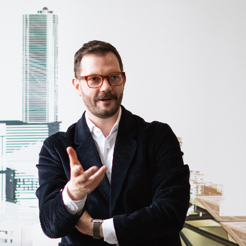 Alphabet's Chief ESG officer Andreas Baron wearing glasses and a dark jacket, gesturing while speaking in a modern office.