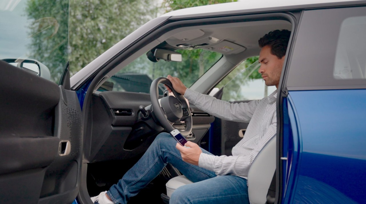 Hombre saliendo de su coche aparccado mientras mira su telefono