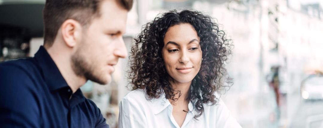 chica de pelo rizado y chico  observando una pantalla en frente suyo