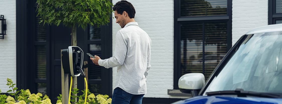 chico sonriendo mirando el movil al lado de un puesto de recarga