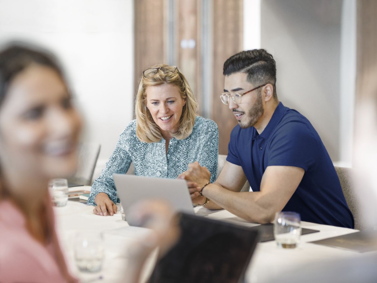 Hombre y mujer en sala de reuniones mirando un ordenador y una chica delante sonriendo