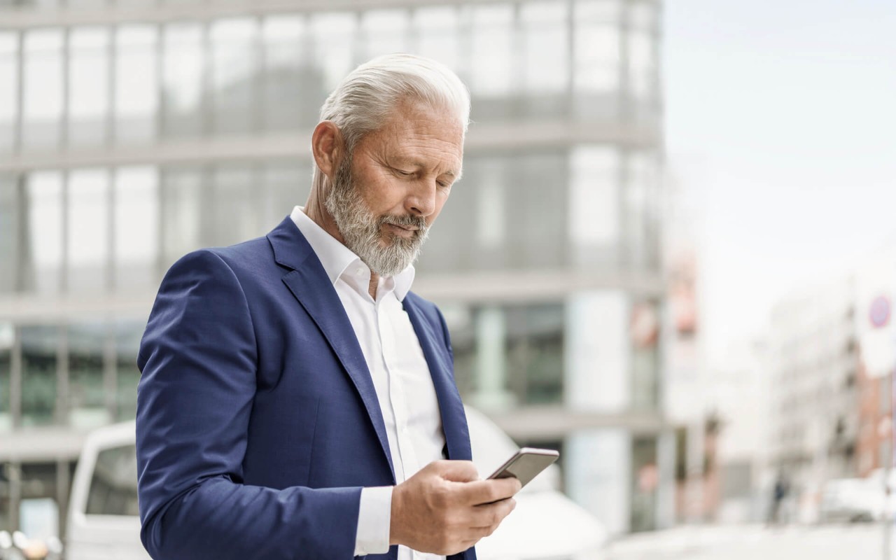 Hombre trajeado mirando su telefono en una zona de oficinas modernas