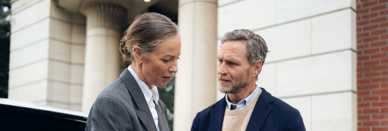 Mujer hablando con un hombre y mostrando puntos concretos de los papeles que estan revisando.