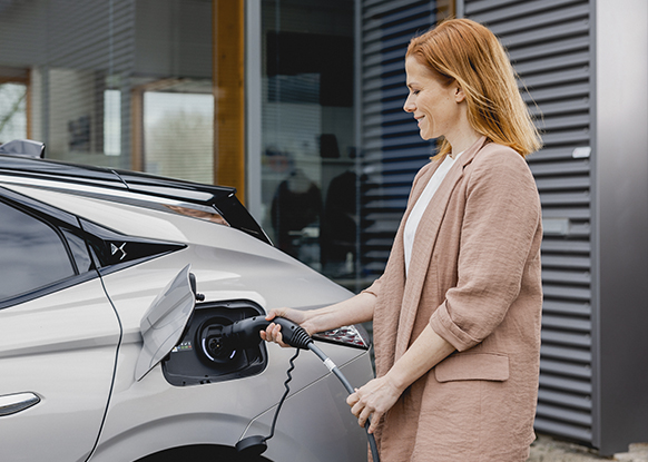 Mujer cargando su coche eléctrico gris.