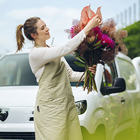 Mujer admirando un ramo de flores delante de su furgoneta blanca, un dia de sol Mujer sujetando un ramo de flores con un delantal