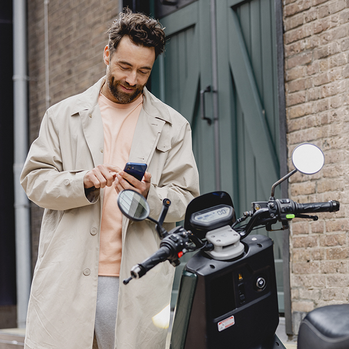 Chico mirando el movil al lado de una moto