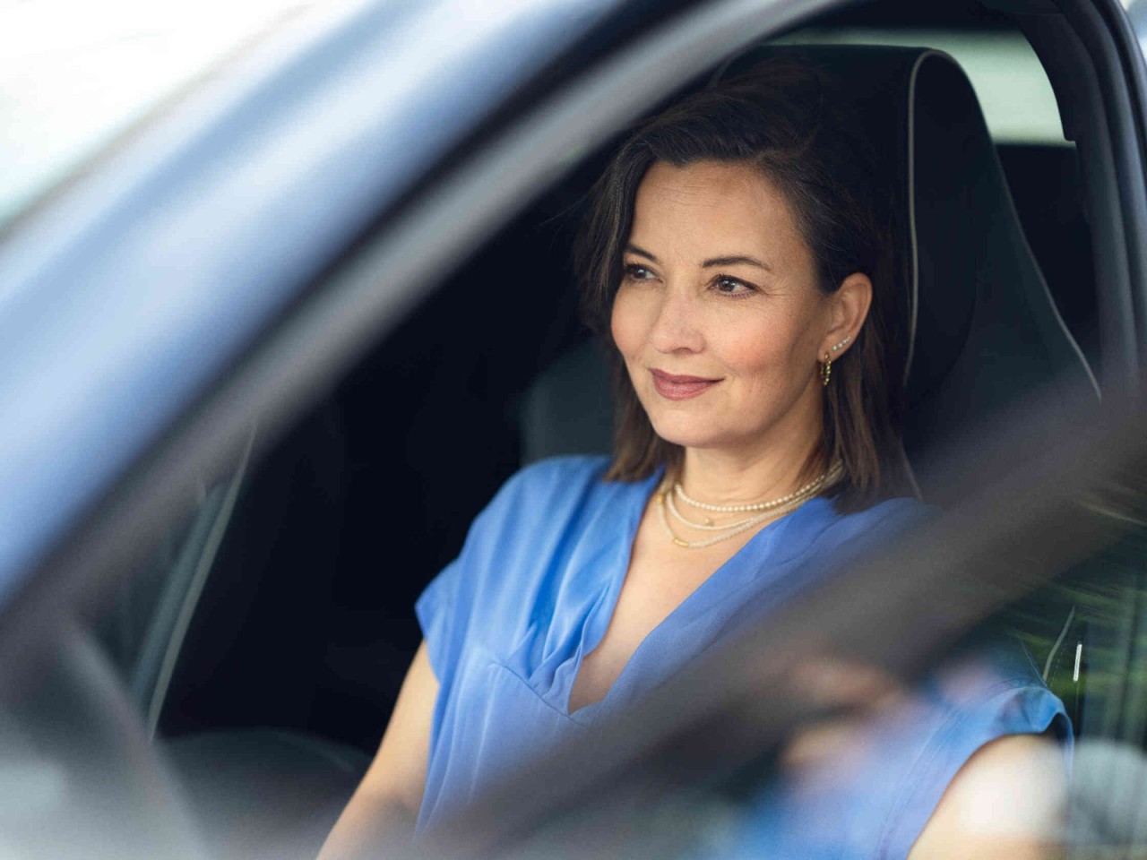 Mujer dentro del coche con la puerta abierta sonriendo en su camiseta azul.