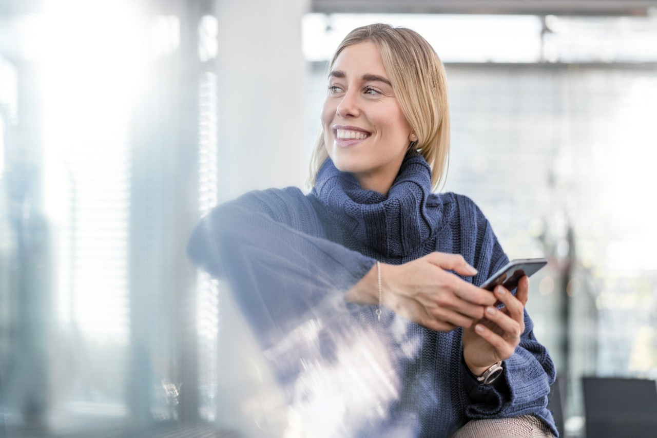 1193069350 chica con jersey azul sujetando un movil y riendo