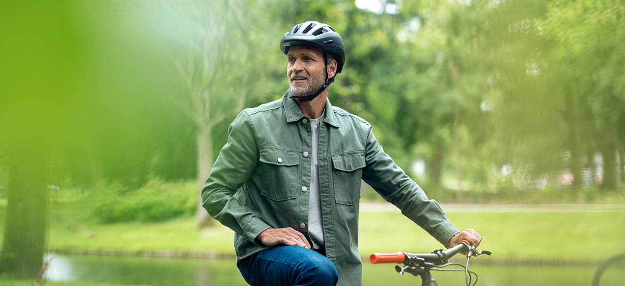 Hombre en bicicleta por un parque con casco