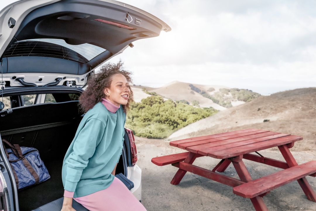 Mujer sentada en la parte de atr'as del coche con una mesa de picnic al lado en medio de la naturaleza. Mujer sentada en la parte de atr'as del coche con una mesa de picnic al lado en medio de la naturaleza.
