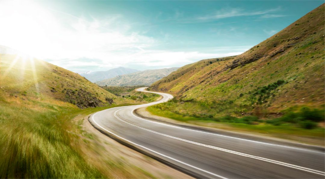 Carretera en medio de monta;as con el sol radiando y el cielo azul.