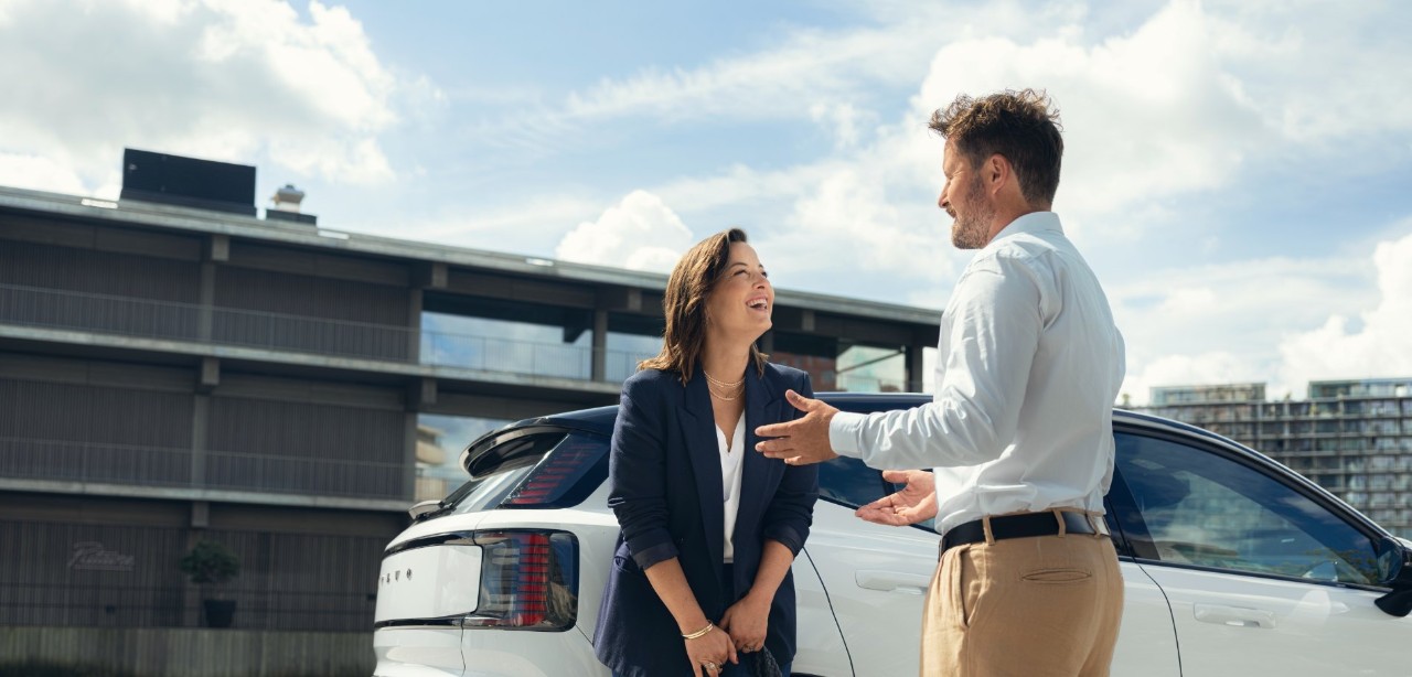 Une femme s'appuie contre une voiture blanche et discute avec un homme.