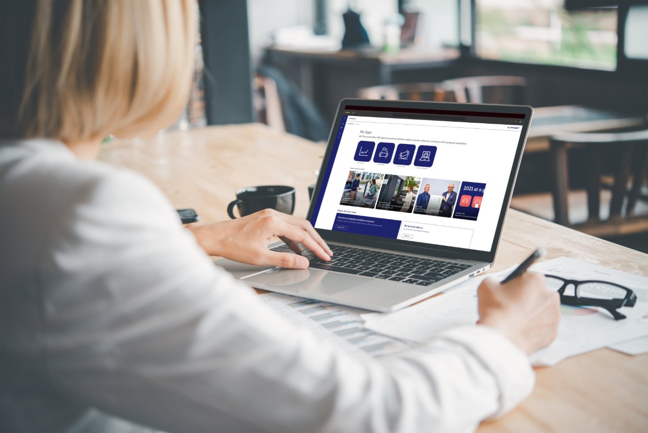 Personne utilisant un ordinateur portable à un bureau dans un bureau moderne, interagissant avec la plateforme numérique Alphabet affichée à l'écran.