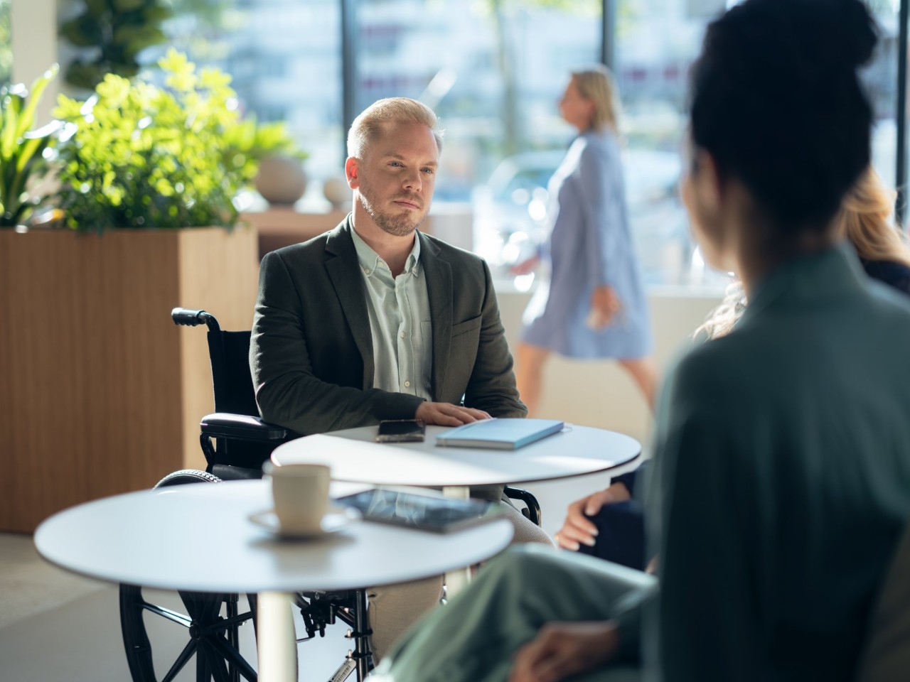 Homme en chaise roulante l'air sérieux parle avec une femme autour d'une table et d'un café
