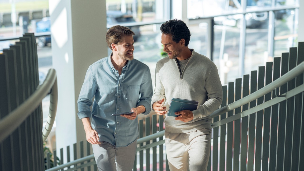 Deux hommes parlent avec un carnet et une tablette à la main en montant des escaliers 