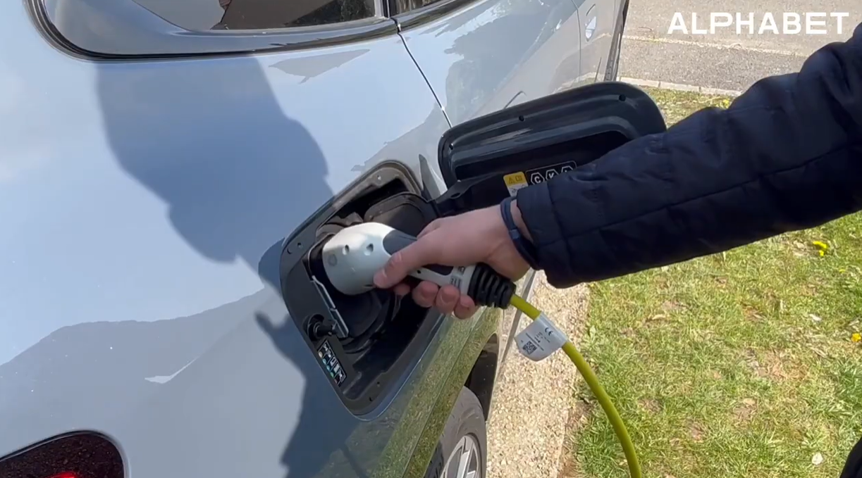 Une main branche une prise électrique à son véhicule garé à l'extérieur