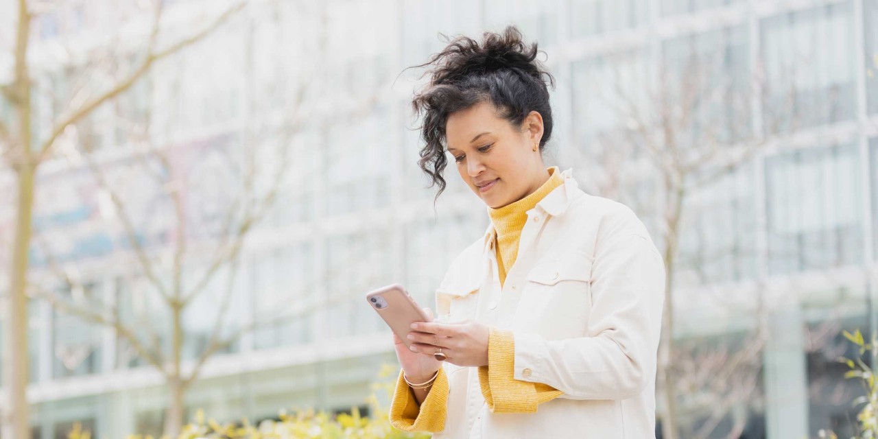 Vrouw met een witte jas kijkt met een glimlach op haar telefoon.