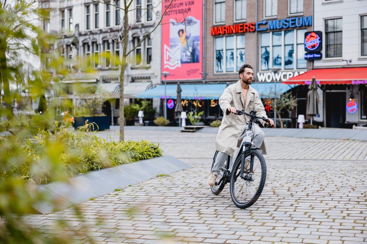 Man met een lange grijze jas zit op zijn fiets.
