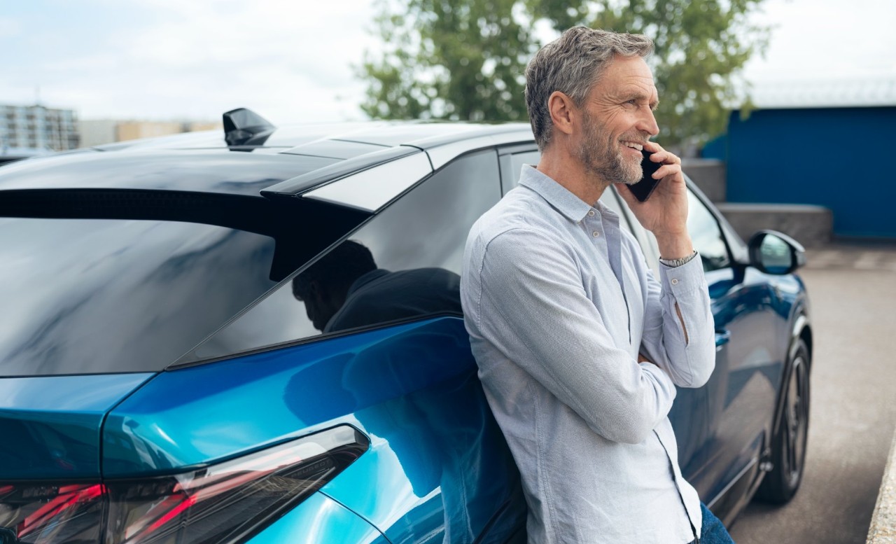 Man belt met zijn telefoon en leunt tegen een blauwe auto aan.