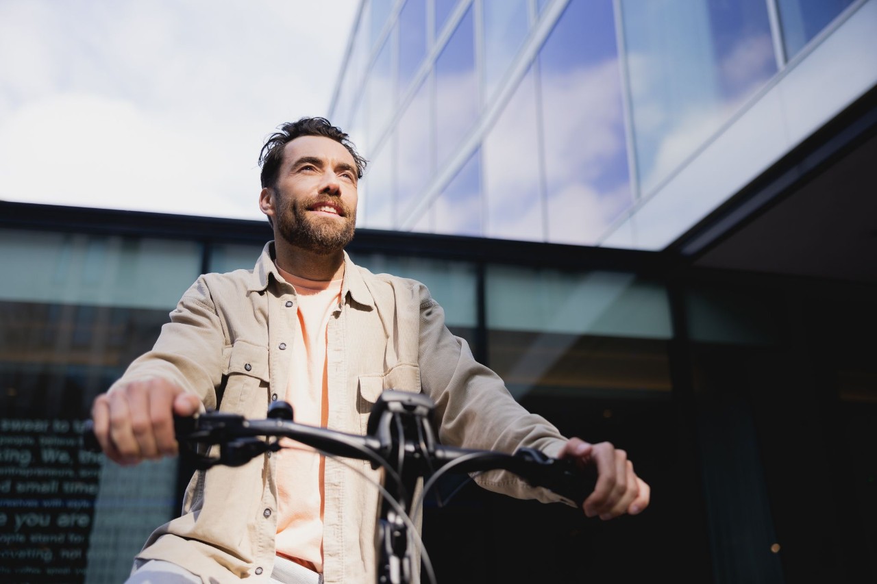 Man met een lange grijze jas zit op zijn fiets.