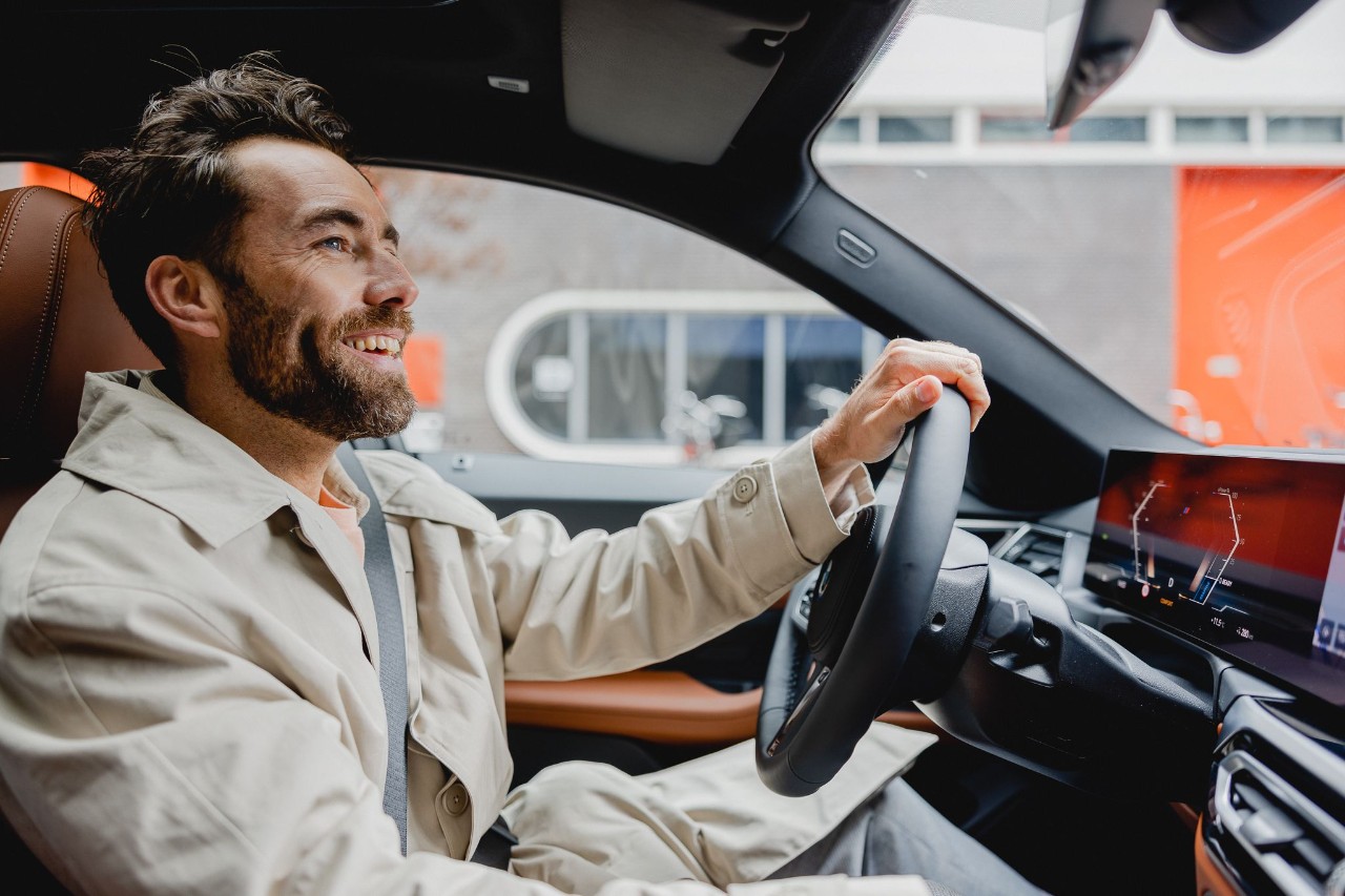 Een man zit alleen in een auto en rijdt met een glimlach.