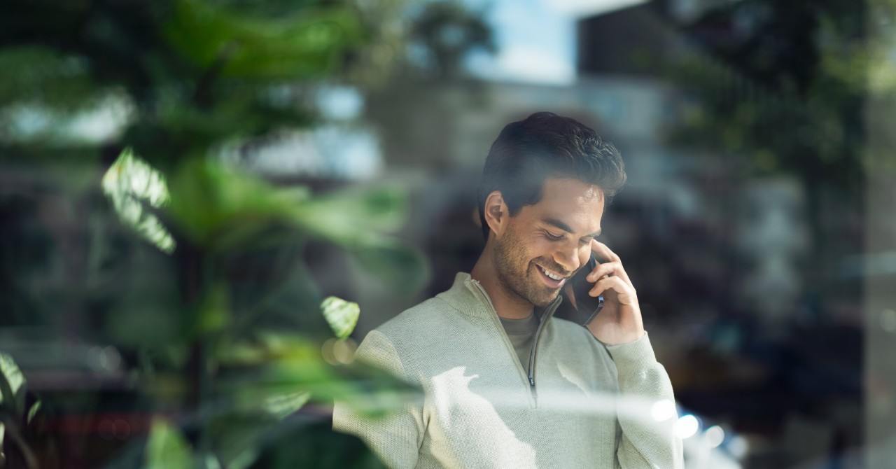 Man die achter een glasplaat aan het bellen is met een smartphone.