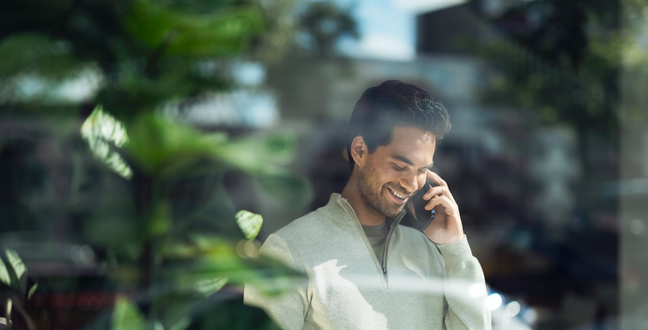 Man die achter een glasplaat aan het bellen is met een smartphone.