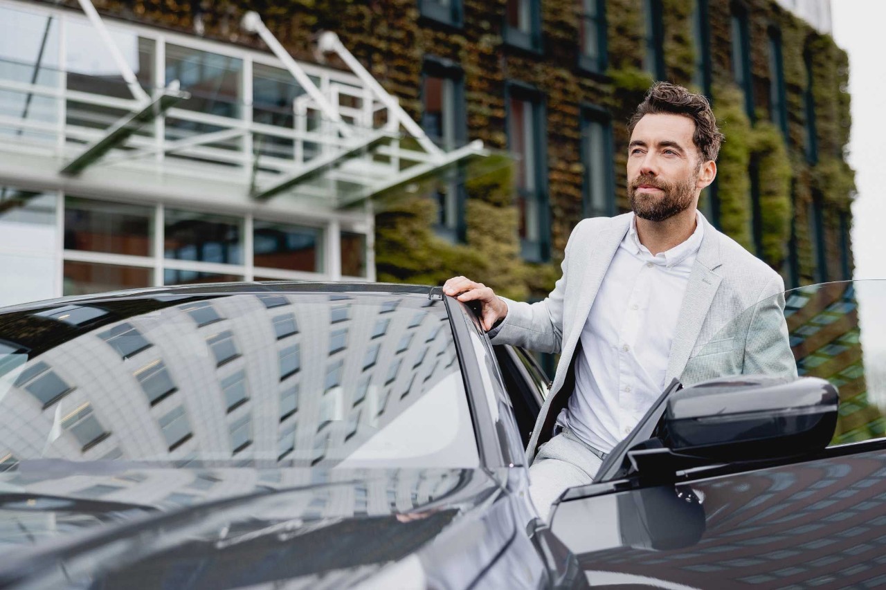 Een man in lichtkleurig pak stapt in zijn auto.