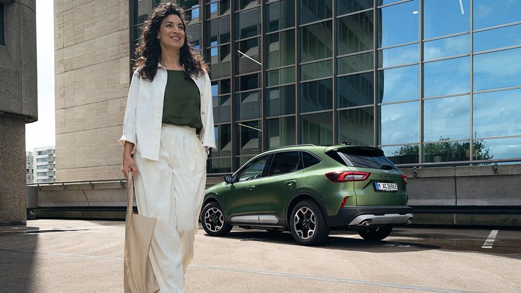 Vrouw loopt met een wit jasje langs een groene Ford.