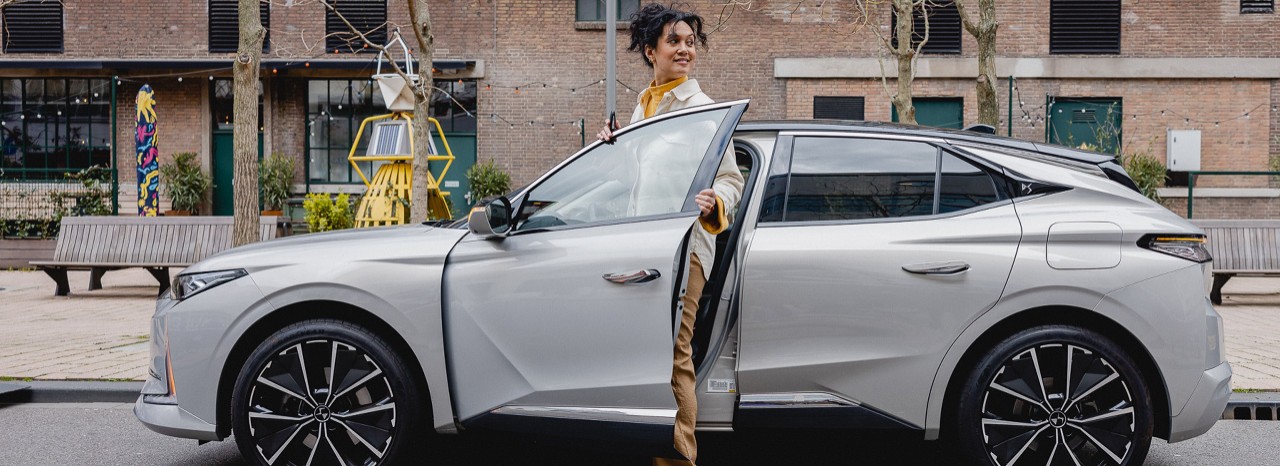 Vrouw in een witte jas stap uit haar geparkeerde auto.