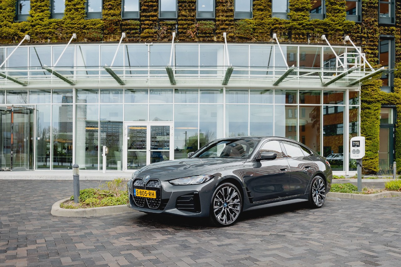 Een zwarte BMW i4 voor een glazen gebouw