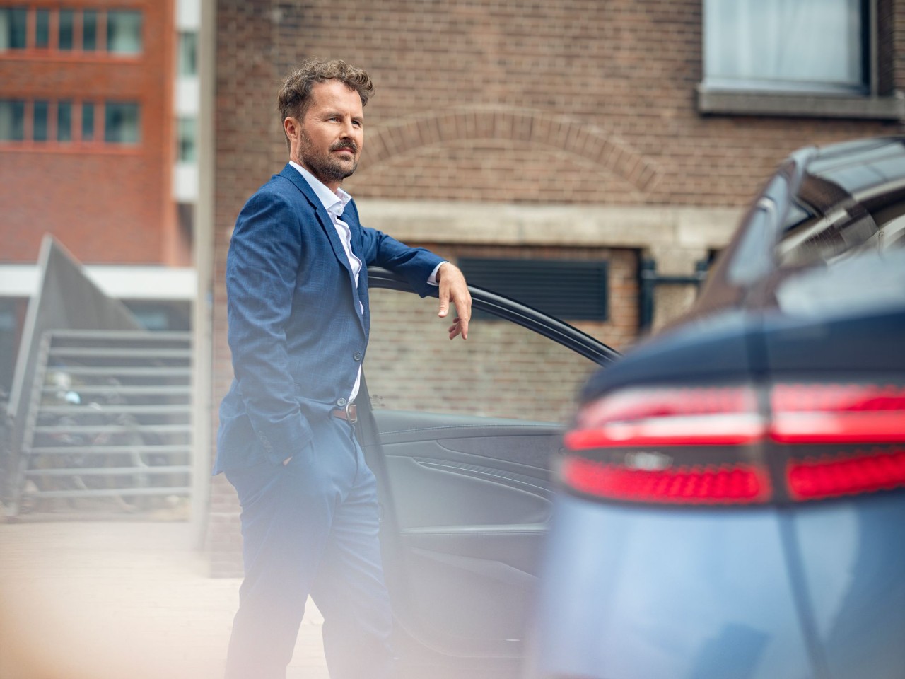 Man leunt met zijn linkerarm tegen de portier van zijn auto.
