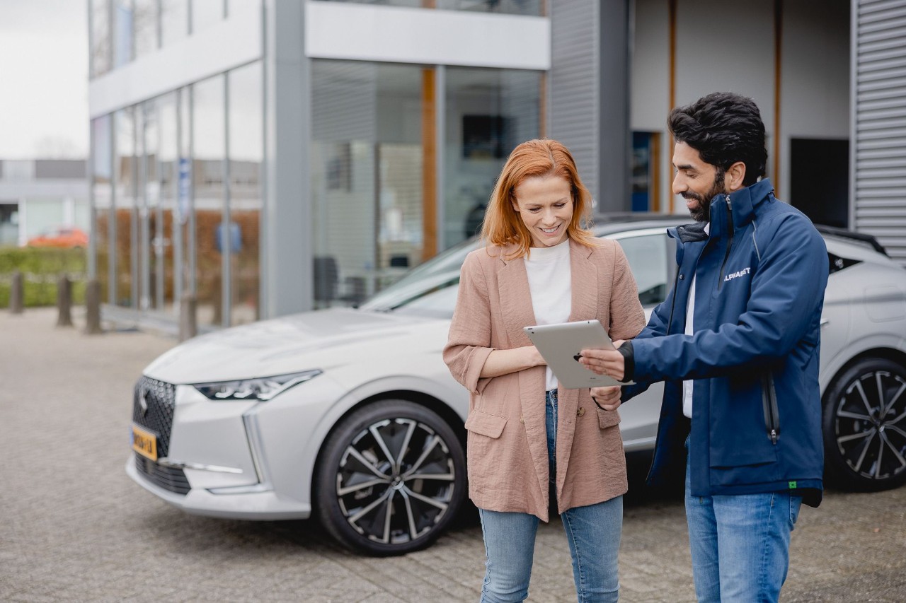 Een medewerker van Alphabet praat met een klant bij een grijze auto.