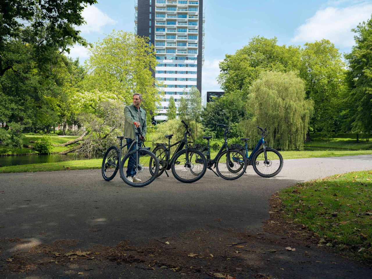 Man staat naast meerdere fietsen in het park met groene landschap modern gebouw op de achtergrond.