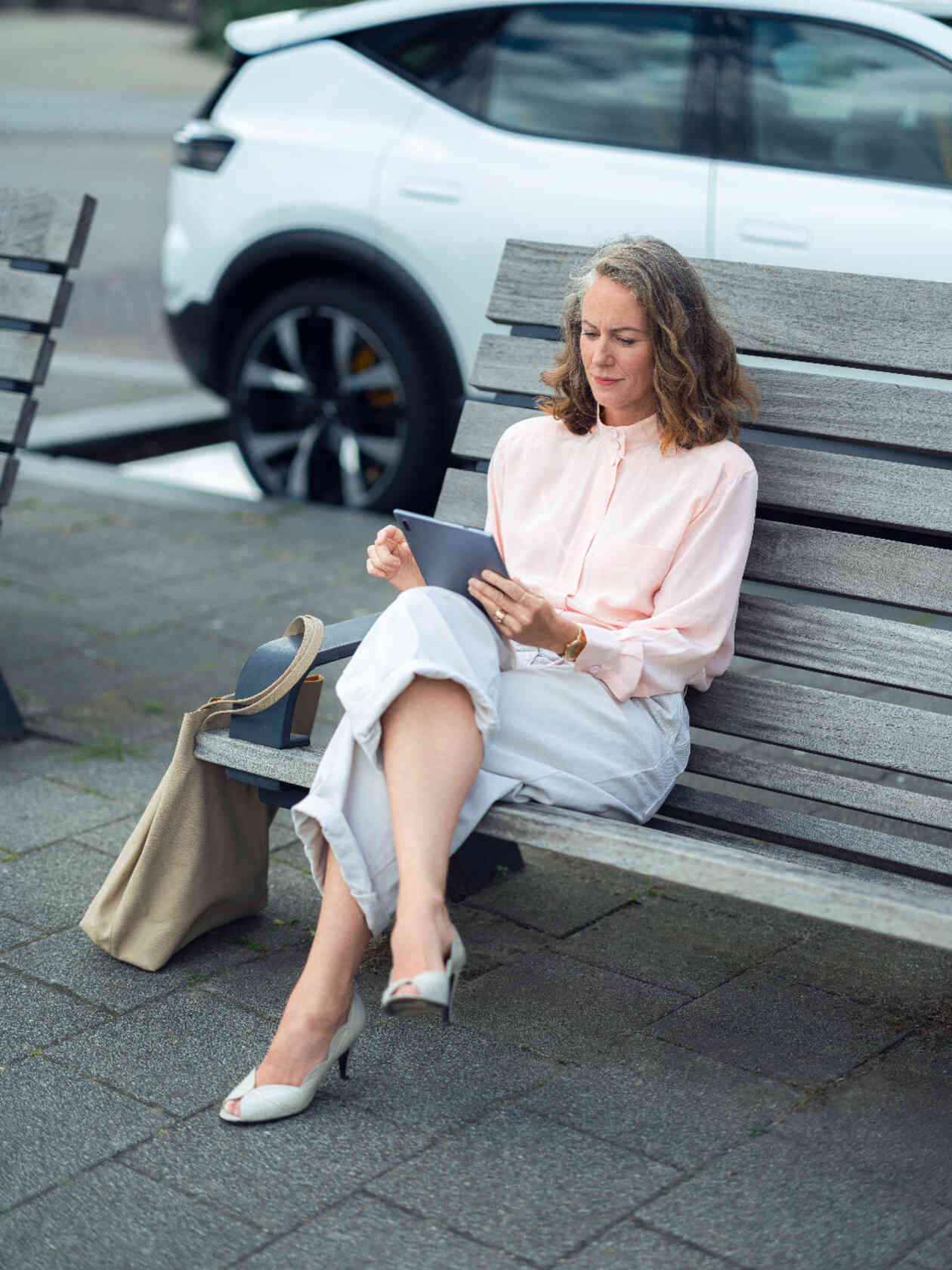 Vrouw zit op een bank met een tablet met een witte auto op de achtergrond.