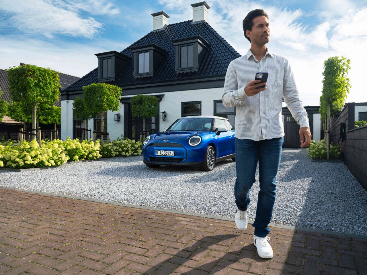 Man-telefoon-oprit Man komt met een telefoon in de hand de oprit af blauwe MINI-auto op de achtergrond.