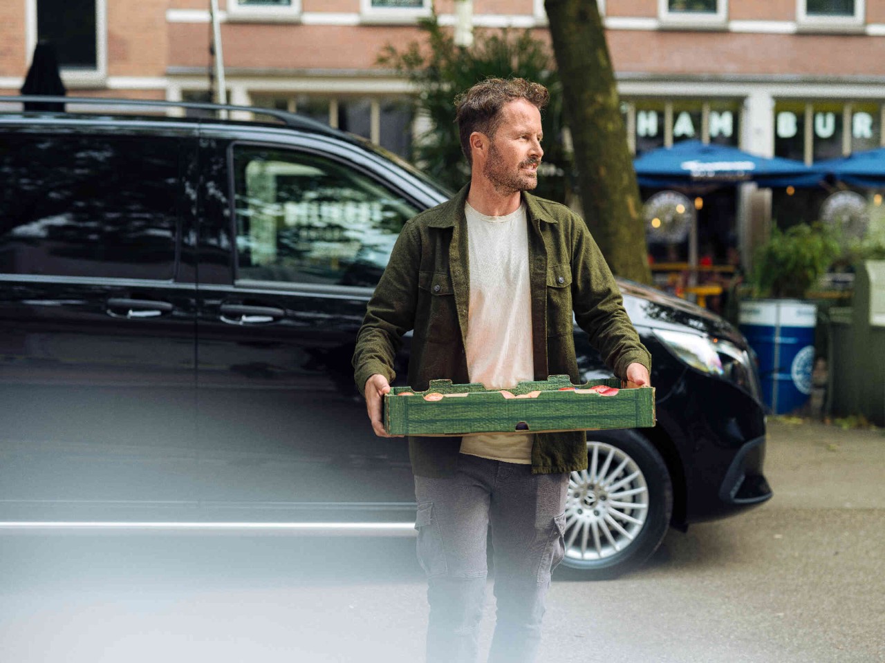 Man loopt met een appelmand over de straat achtergrond toont een zwarte bestelwagen.