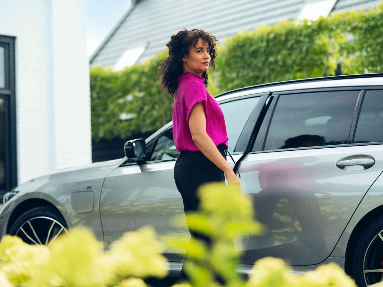 Vrouw sluit de deur van een grijze auto in een oprit.