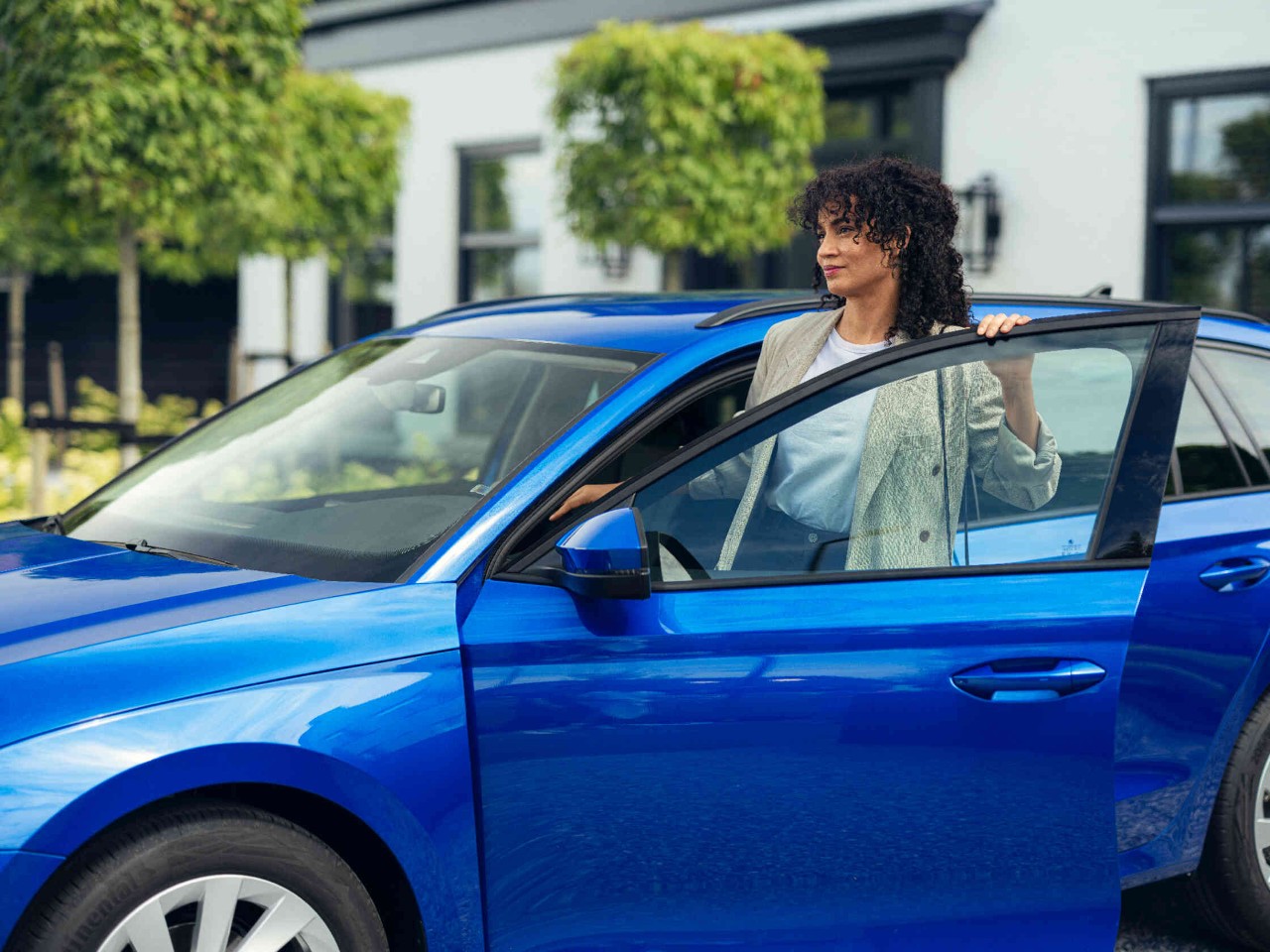 Vrouw stapt uit een blauwe auto voor een modern gebouw.