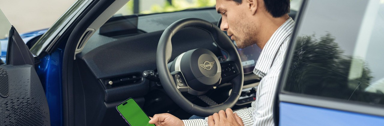 Man kijkt op zijn telefoon in een MINI met een geopende portier.