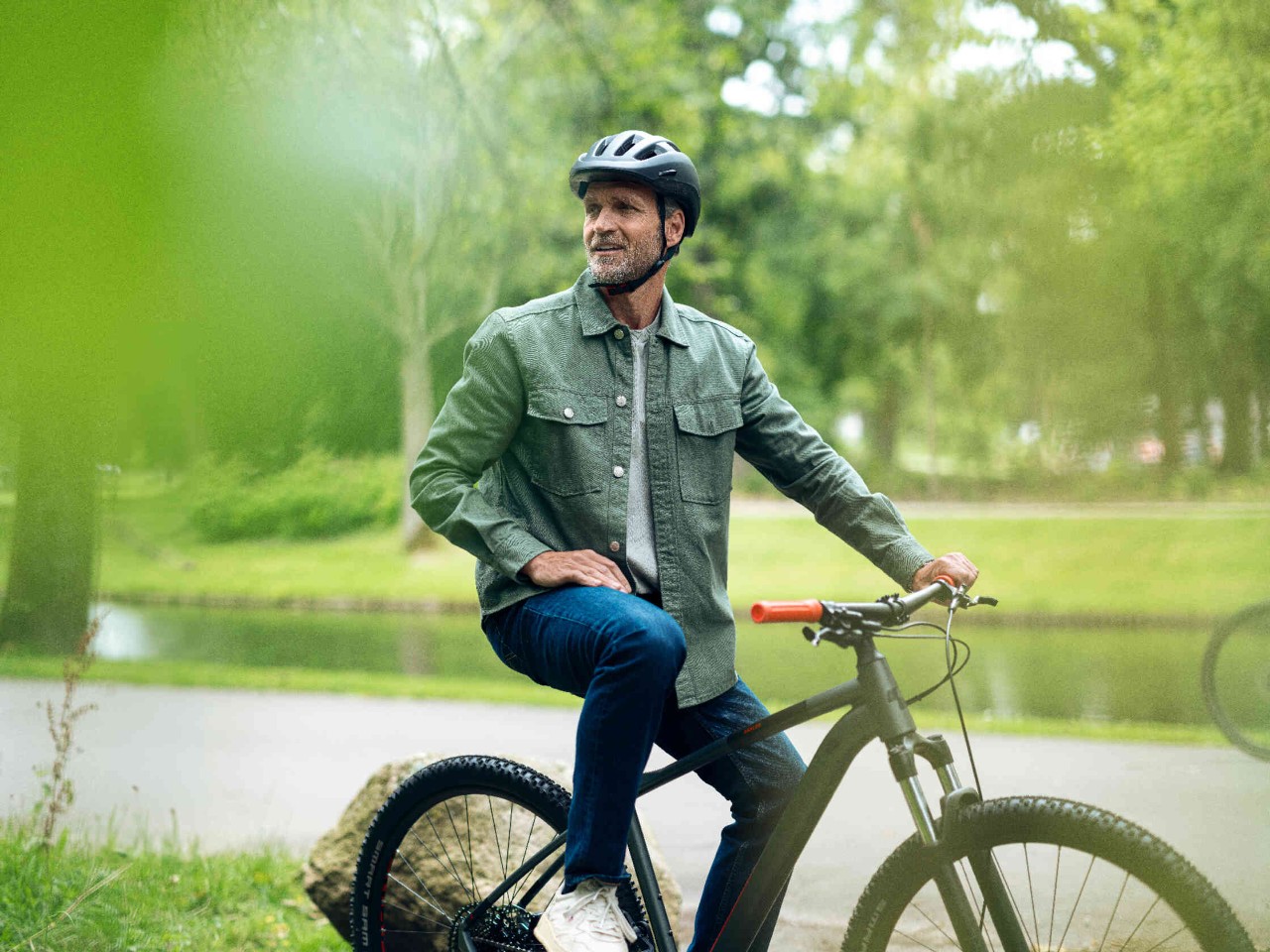 Man op mountainbike in een groen park met een beek op de achtergrond.