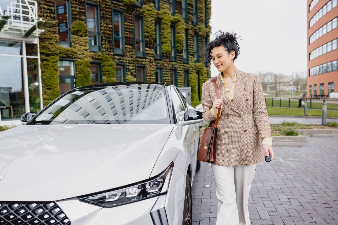 Vrouw loopt naast haar witte auto.