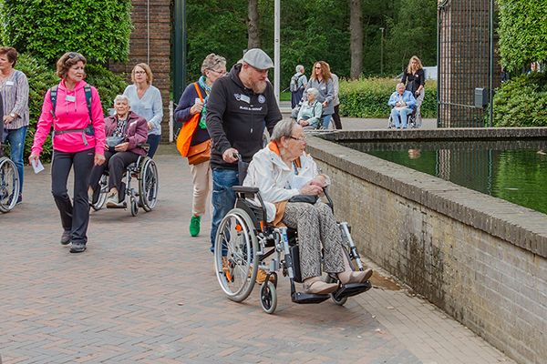 Groep jongeren en ouderen mensen waarvan de jongeren de oude mensen duwen die in een rolstoel zitten