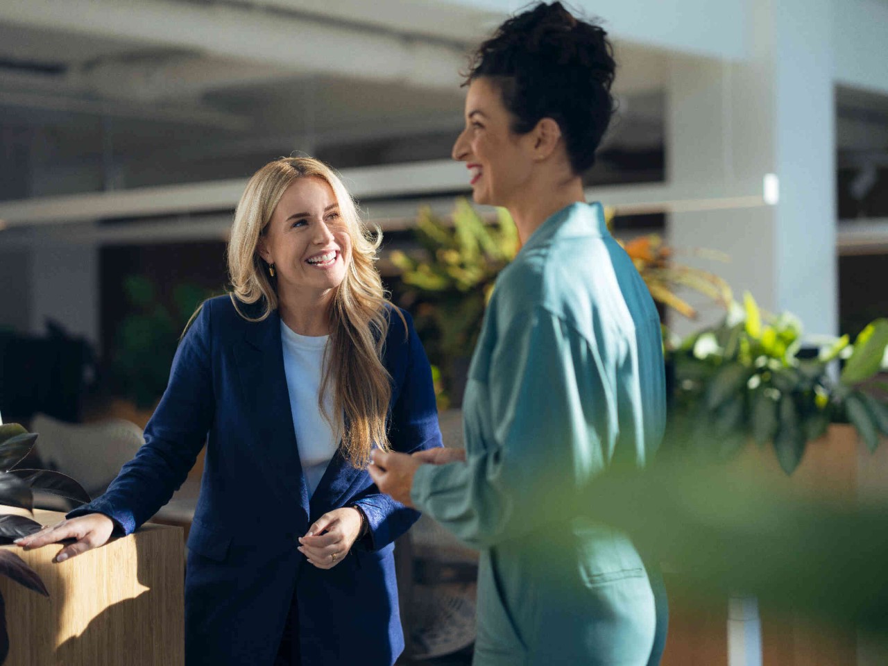 Twee vrouwen praten en lachen in een lichte ruimte met planten.