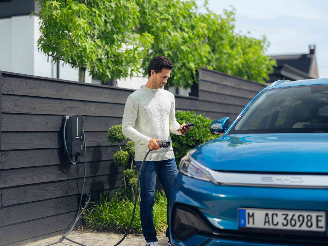 Man staat naast een BYD-auto en houdt een laadstekker en telefoon in zijn hand.