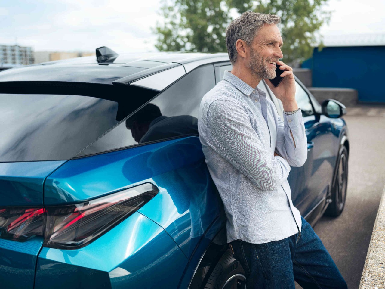 Man leunt tegen een moderne blauwe auto telefoneert met smartphone elegant design.