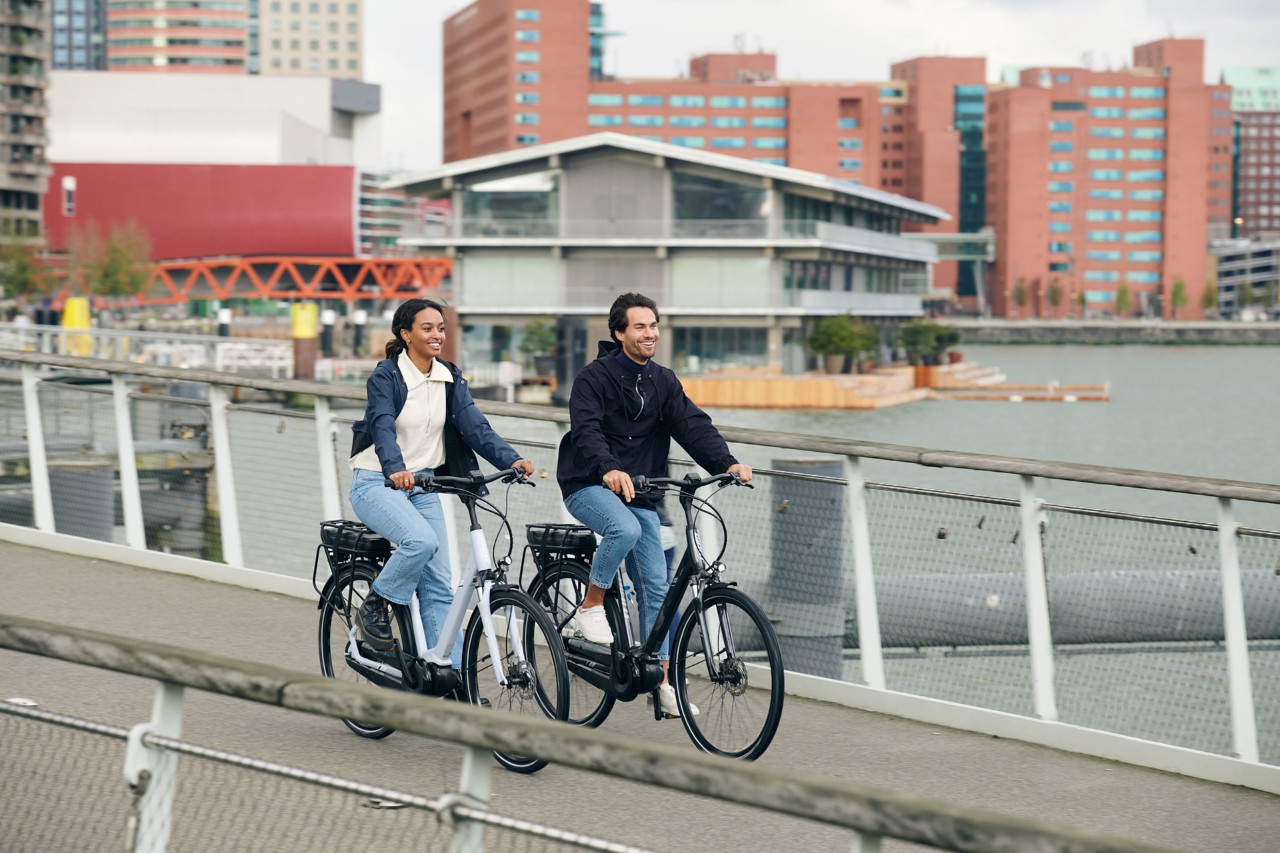 Een man en een vrouw fietsen langs het water in een stad.