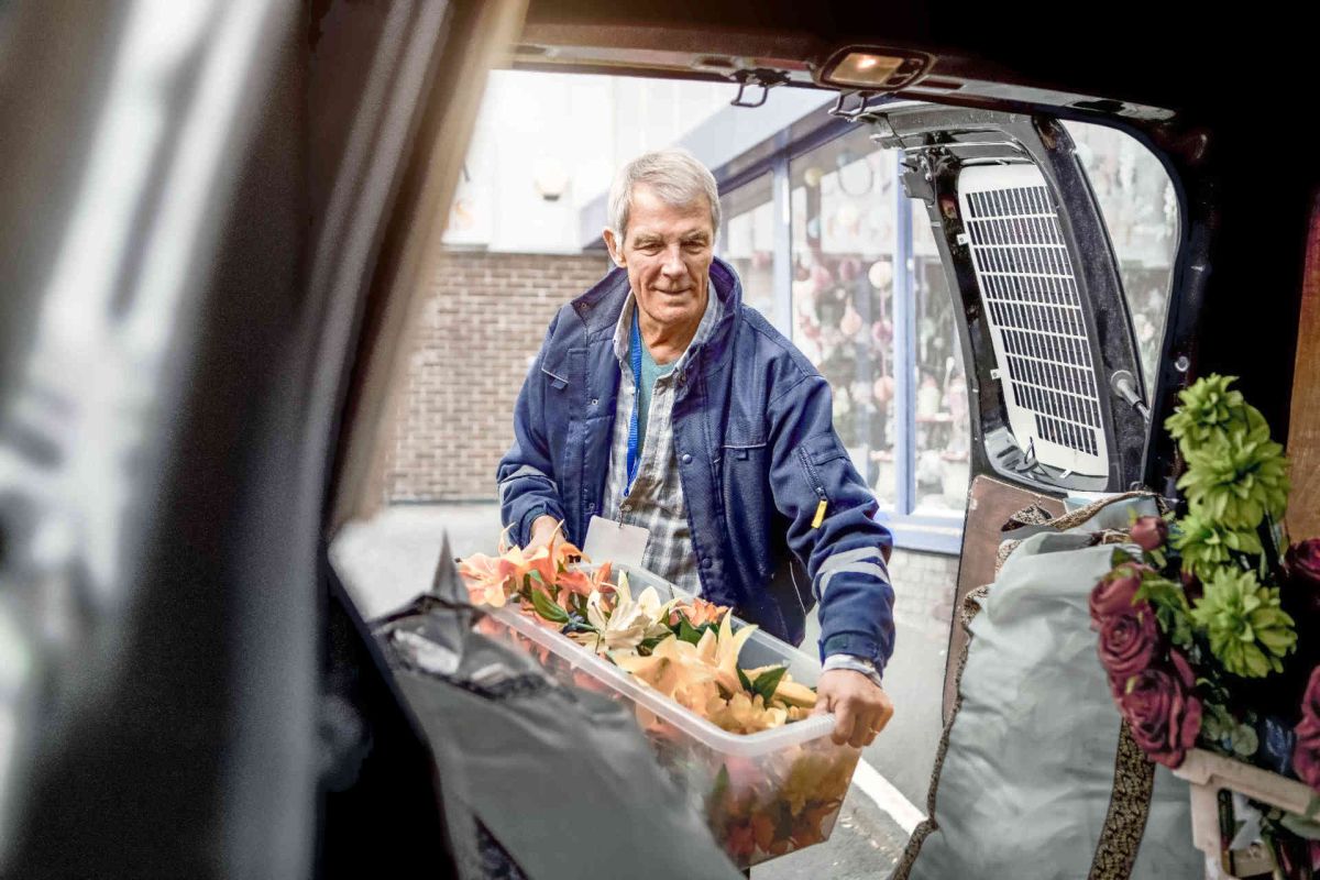 Man met krat in hand bij achterklep van de auto